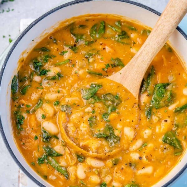 top view of white bean soup in a pot with a wooden spoonful of soup