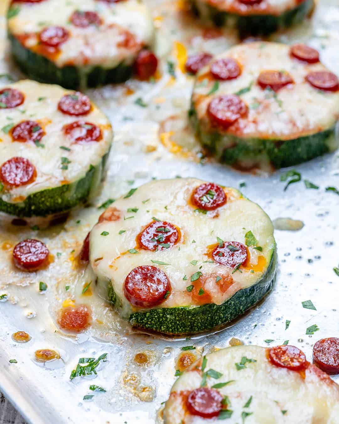 pizza zucchini  bites topped with pepperoni and melted cheese on a sheet pan.